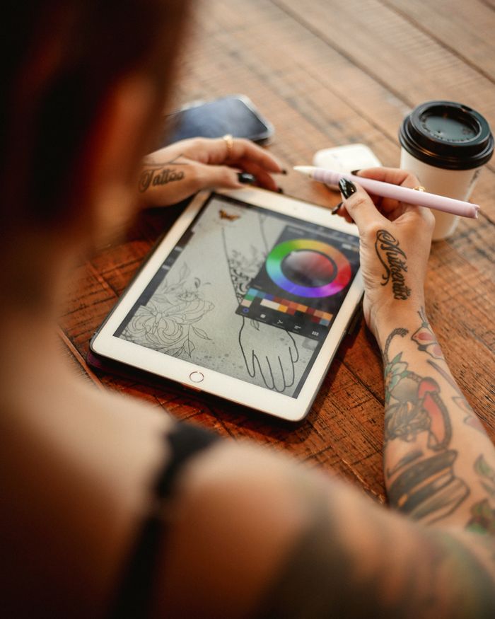 Tattooed artist using tablet and stylus for digital drawing. Coffee nearby.