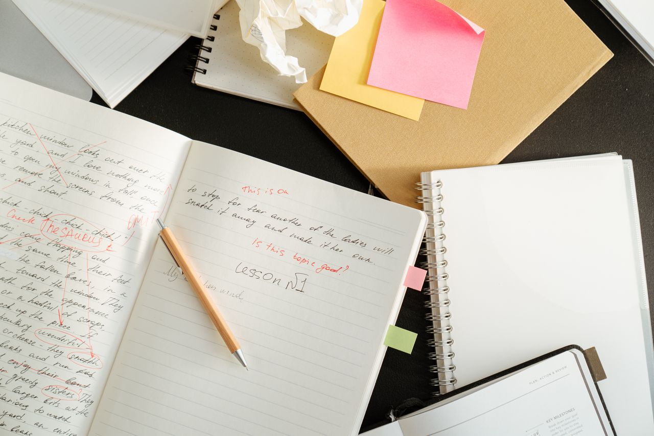 A cluttered desk with notebooks, sticky notes, and stationery for educational purposes.